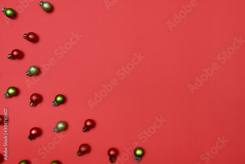 Creative Christmas pattern with red and green shiny baubles on red background, copy space. Minimal, winter, new year concept. Top view, flat lay