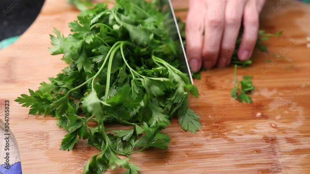 Female hand cutting parsley on a wooden board Female hand cutting parsley on a wooden board