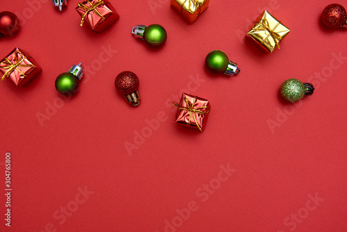 Creative Christmas pattern with red and green shiny baubles and gifts on red background, copy space. Minimal, winter, new year concept. Top view, flat lay
