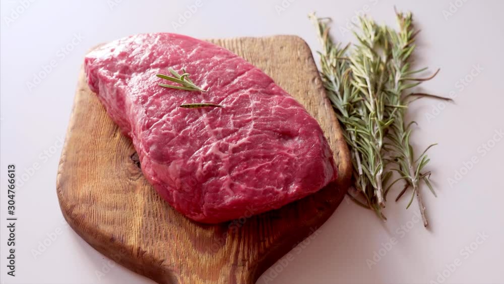 Raw Fresh Steak Served with Rosemary on Rustic Wooden Board on White Kitchen Table. Marble Meat with Ingredients for Cooking Raw Fresh Steak Served with Rosemary on Rustic Wooden Board on White Kitchen Table. Marble Meat with Ingredients for Cooking