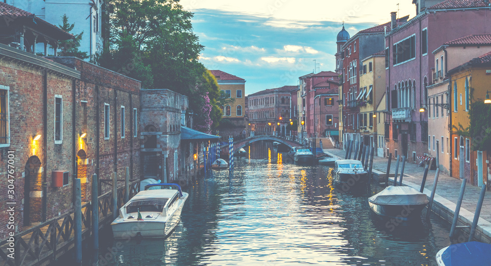 View on canal with boats and colorful facades of old medieval houses in Venice, Italy. Picturesque landscape. Travel to touristic places of Europe. Vintage tone filter effect with noise and grain.