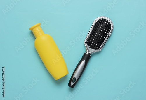 Minimalistic beauty concept. Hair care. Comb and bottle of shampoo on blue background. Top view
