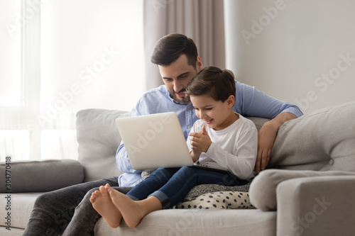 Caring father teaching adorable little son to use laptop