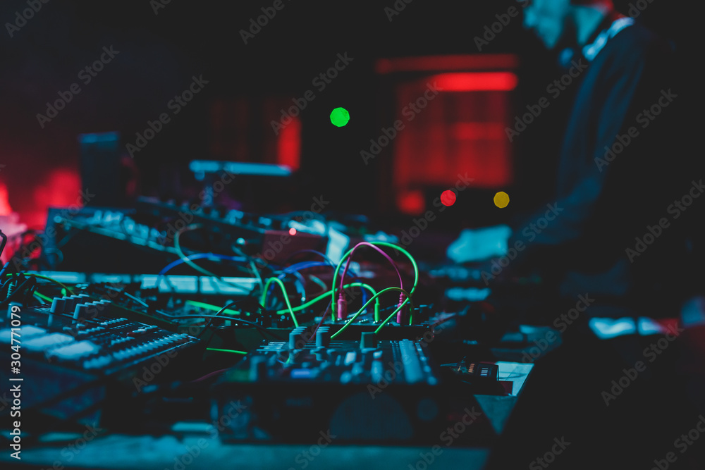 View of Dj mixer and vinyl plate with headphones on a table with DJ playing and mixes the track in the background, during night techno party in the nightclub - obrazy, fototapety, plakaty 