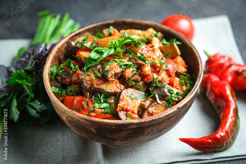 Vegetable saute or caponata, or pisto with eggplant, peppers, tomatoes and herbs in rustic bowl on a dark background.