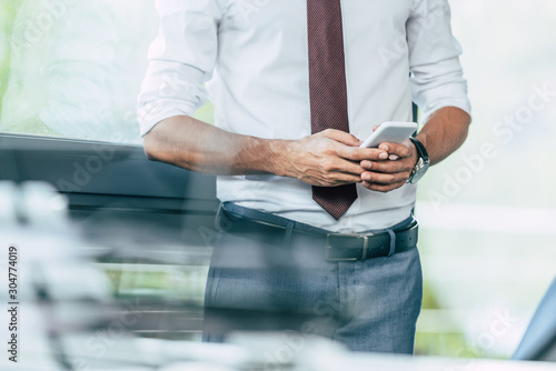 selective focus of businessman using smartphone in office, cropped view