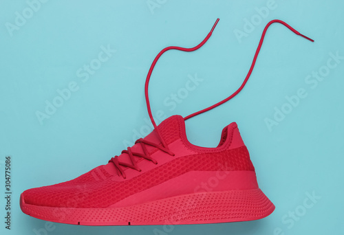 Red sport running shoe with untied laces on blue background. Top view