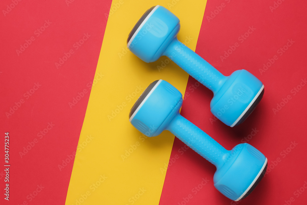 Plastic dumbbells on a red-yellow paper background. Minimalism fitness concept. Top view Plastic dumbbells on a red-yellow paper background. Minimalism fitness concept. Top view