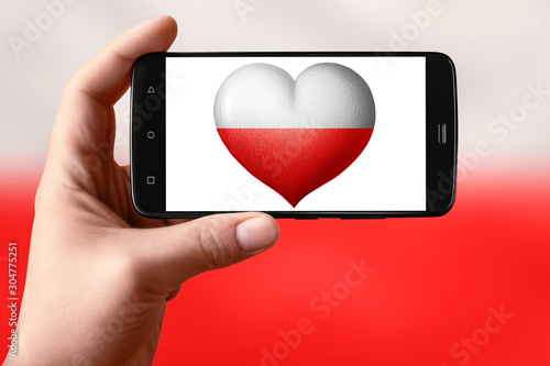 Poland flag in the shape of a heart on the phone screen. Smartphone in hand shows a heart flag. photo