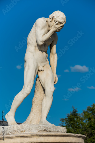 Cain Statue in Tuileries Garden in Paris, one of many statues in the Tuileries Garden. It shows a naked man (Cain) standing or propped awkwardly with his right hand covering his face.