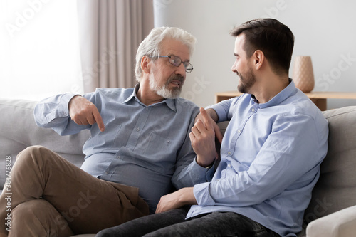 Old father talking with son, having pleasant conversation at home