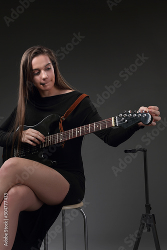 Beautiful girl tuning strings on electric guitar