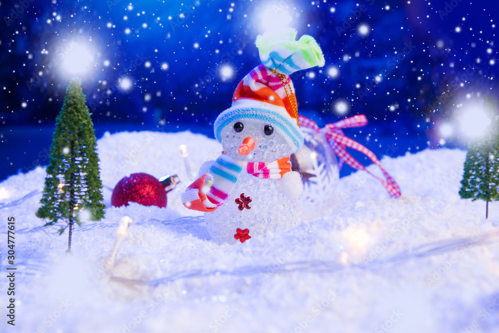 Snowman with Christmas balls on snow over fir-tree, night sky and moon. Shallow depth of field. Christmas background. Fairy tale. Macro. Artificial magic dreamy world.