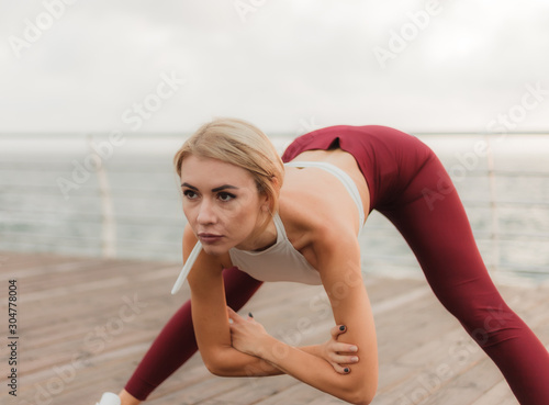 Morning workout. Healthy lifestyle concept. Young attractive woman in sportswear does warm up before exercise on the beach at sunrise. Stretching