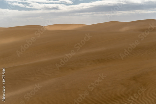 Amazing sand dunes during sunny and windy day in the Natural Reserve of Dunes of Maspaloma in Gran Canaria with sand dust, Canary Islands, Spain