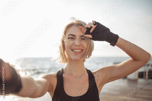 Selfie portrait of a young cheerful fitness woman on the beach at sunrise