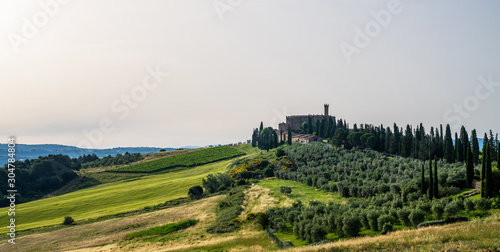 Tuscany rural sunset landscape. Countryside farm, cypresses trees, green field, sun light and cloud. Italy, Europe.