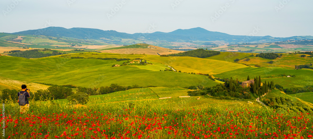 Famous popular tourist place in the world. Tourist in Tuscany visiting landmark sightseeing in Italy, taking photo. Countryside landscape with red poppy flowers.