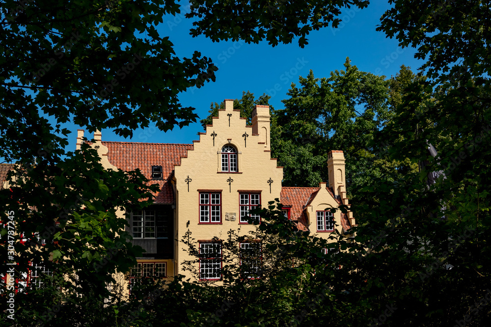 House hiding behind the branches. Framed street view of beautiful historic city center architecture of Bruges or Brugge, West Flanders province, Belgium. Lovely summer August weather