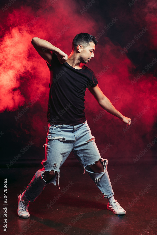 Young man professional dancer fond of dancing. dancing movements by caucasian man isolated in studio with red smoky background