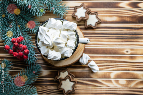 Beautiful Christmas or New Year composition with cup of hot cacao drink with marshmallows, sweet cookies, fir tree branches and decor on dark wooden background with bokeh lights. 