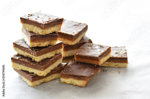Millionaire's shortbread with chocolate and caramel on a parchment paper with copy space on the right side.