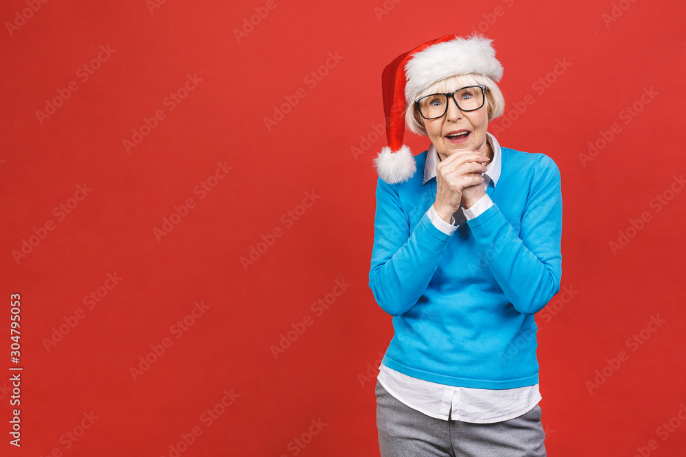 Senior aged grey-haired woman wearing Christmas Santa hat over isolated red background very happy and excited, having fun, smiling. Senior aged grey-haired woman wearing Christmas Santa hat over isolated red background very happy and excited, having fun, smiling.