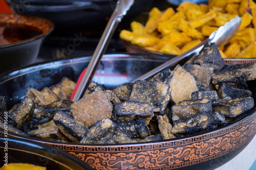 Black Chinese Stinky Tofu in Big Plate Seen from China Local Street Market. Deep Fried (Yellow) Stinky Tofu Blurred at Background. photo