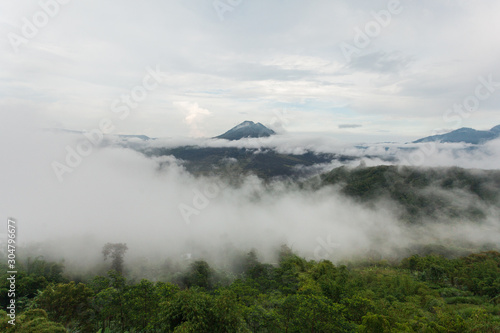 Dramatic picture with fog over the jungle. A volcano is visible in the distance.
