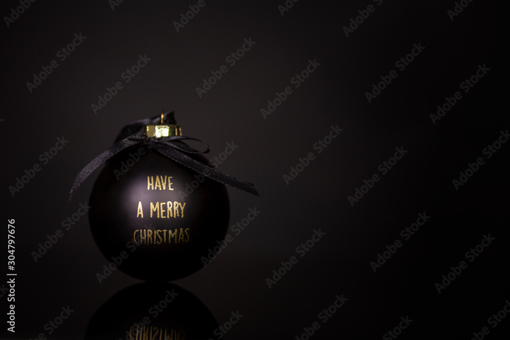 Black Christmas ball with congratulations in gold letters on a black background. Space for text. Close-up.