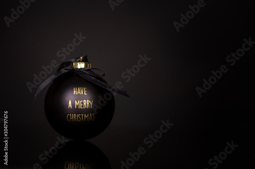 Black Christmas ball with congratulations in gold letters on a black background. Space for text. Close-up.