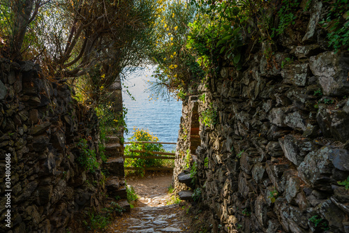 Looking through a narrow medieval street with stone wall at the blue sea and sky.