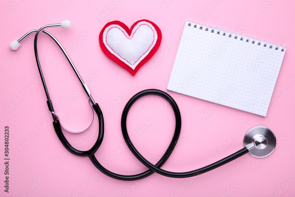 Stethoscope with notebook on pink background. Top view with place for your text.