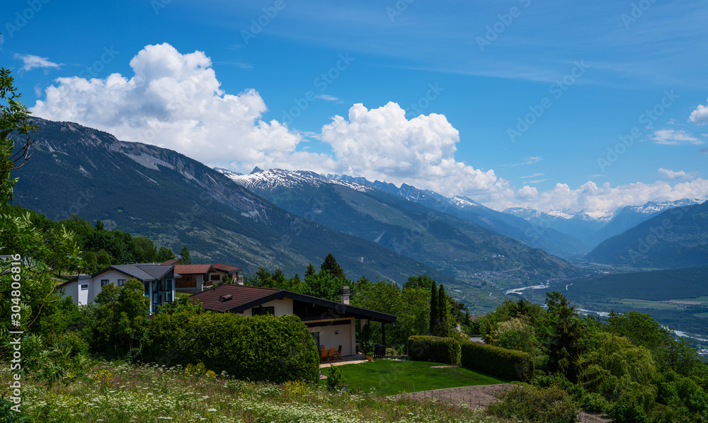 Stunning alpine panorama colorful summer view. Beautiful outdoor scene Switzerland, Europe. Hazy blue mountains. Alpine houses, meadows on the slopes and snow-capped mountains.