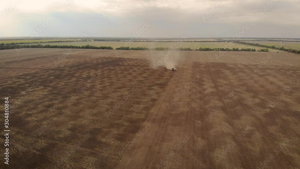 Aerial view of tractor with harrows working on field cultivating dry soil leaving haystack of dust behind. Drone sliding shot of agricultural machinery with rotary plow prepares land for sowing Aerial view of tractor with harrows working on field cultivating dry soil leaving haystack of dust behind. Drone sliding shot of agricultural machinery with rotary plow prepares land for sowing