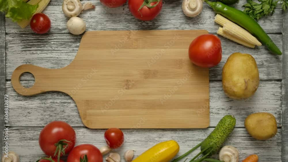Male hand swirling tomato on cutting board. Various vegetables such as cucumber, potatoes, chili peppers, paprika, mushrooms on the table. Male hand swirling tomato on cutting board. Various vegetables such as cucumber, potatoes, chili peppers, paprika, mushrooms on the table.