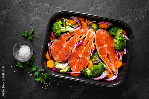 Salmon. Cooking fresh raw salmon fish steaks with vegetables, broccoli, carrot and onion on black background, top view