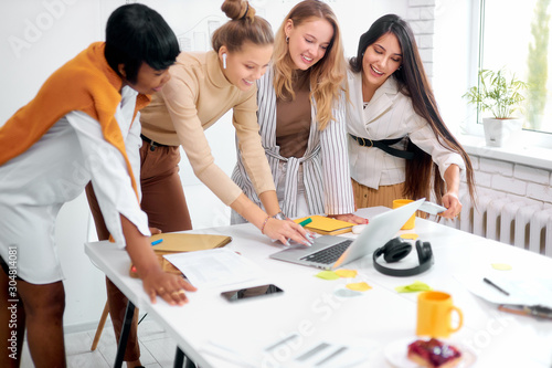 cheerful business people in office, positive process of coworking, young ladies of caucasian and african apperance together work photo