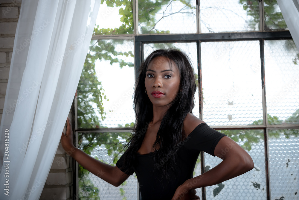 vertical image african american woman wearing lingerie in front of window. Sheer lace curtains and ivy in background. Soft subtle and romantic. 