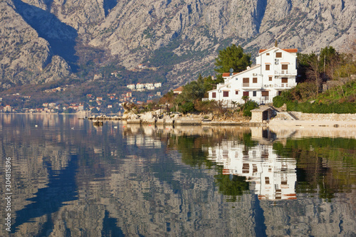 Winter Mediterranean landscape. Mountains and town are reflected in water. Montenegro, Adriatic Sea, Bay of Kotor, Dobrota town