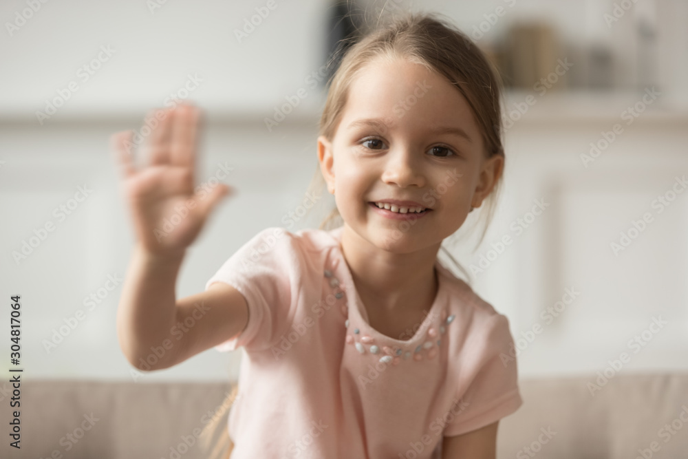 Little preschooler girl sit on couch waving looking at camera Little preschooler girl sit on couch waving looking at camera
