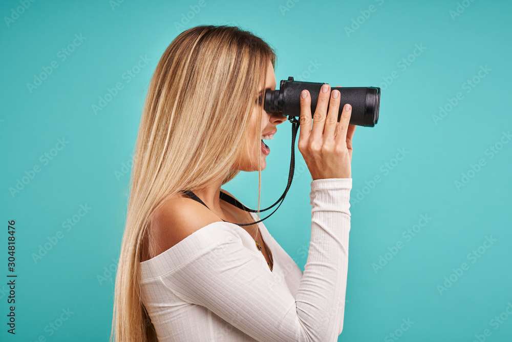 Beautiful adult woman posing over blue background with binoculars Beautiful adult woman posing over blue background with binoculars