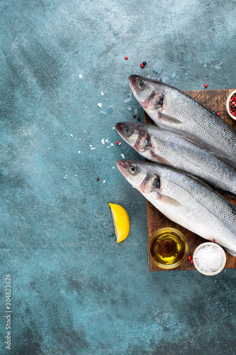 Photography Fresh sea bass fish and lemon, olive oil, salt, pepper on turquoise grunge background