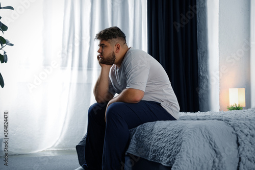 Depressed overweight man on bed at home photo