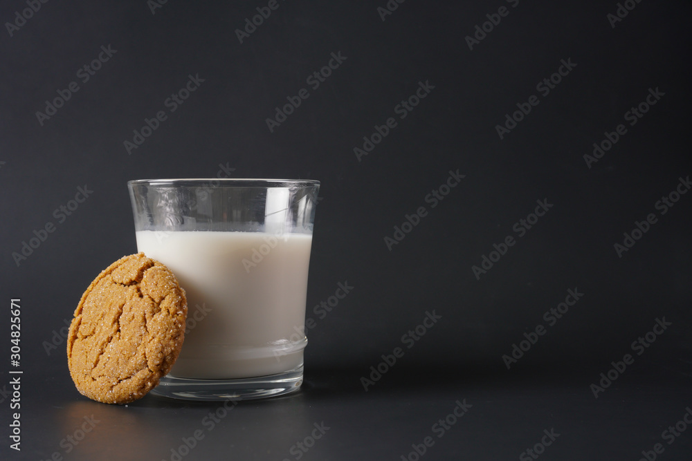A gingerbread cookie leans up against a glass of cold milk on a black background with copy space A gingerbread cookie leans up against a glass of cold milk on a black background with copy space