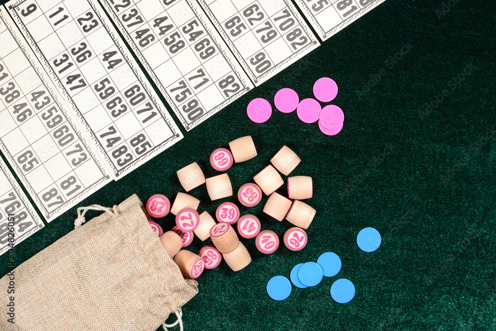 Lotto, classic family board game. Some wooden barrels, blue chips and cards on green velvet surface. Vintage game, bingo. Lotto, classic family board game. Some wooden barrels, blue chips and cards on green velvet surface. Vintage game, bingo.