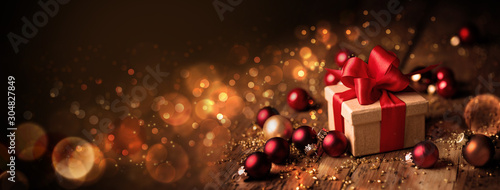 Abstract Christmas Banner  -  Gift box with red bow and baubles on wood  -  Magic dark golden bokeh lights background