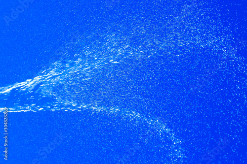 Blurred in motion jet of water on a blue background. Brilliant spray.