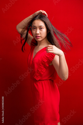 Dynamic shot of young beautiful Asian appearance kopeck piece in a red dress dancing on a red background