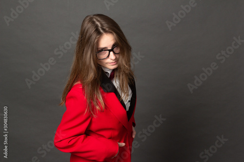 angry girl in white shirt, black vest and red jacket with Burgundy bow tie and classic black pants office style and glasses on gray background © Roman Kornev